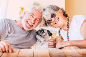 Cheerful old senior couple smile and enjoy her best friend dog pug with love - concept of happy mature people and animal - joy retired elderly lifestyle